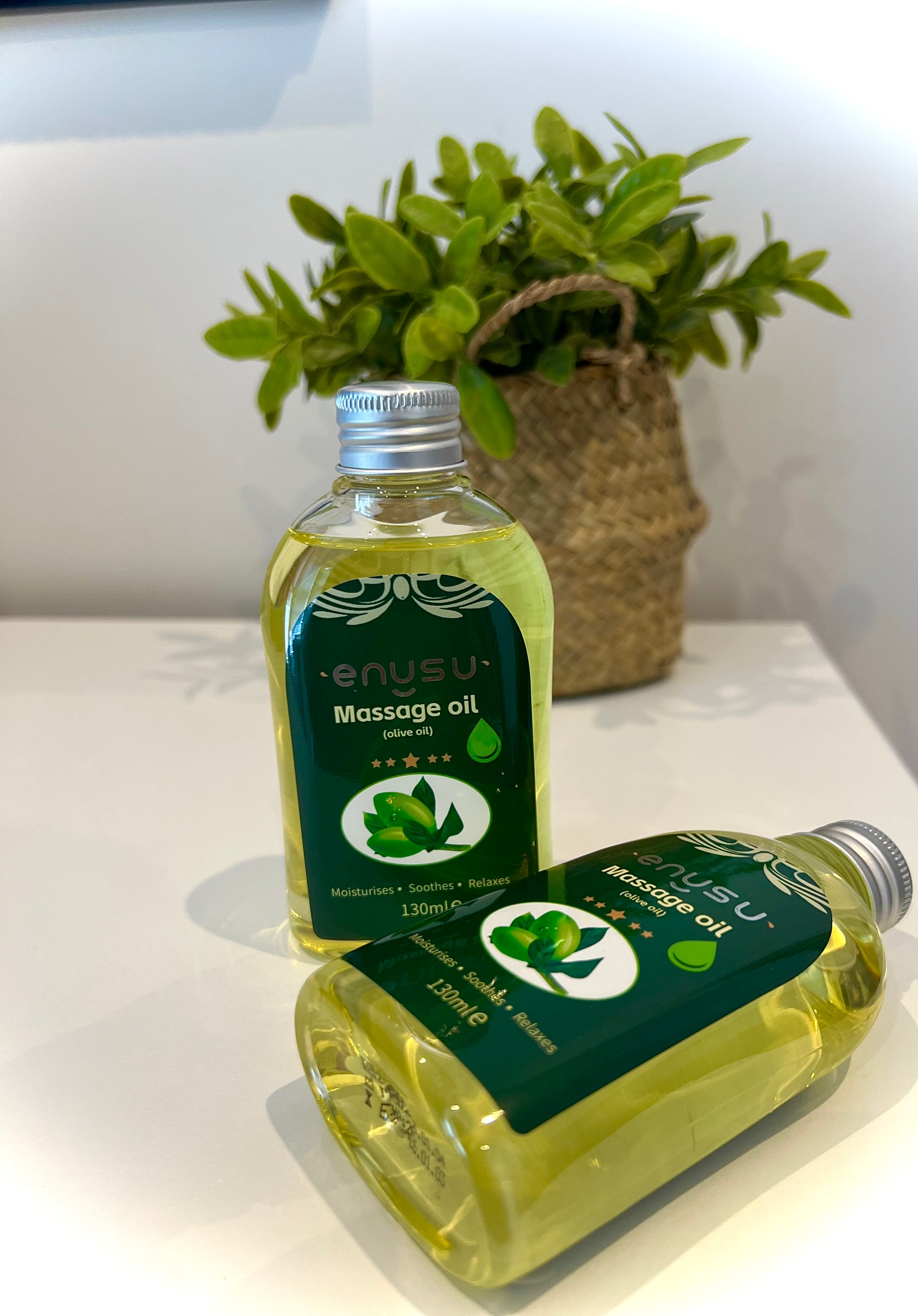 Two bottles of Enusu LADYBLOOM massage oil on a white surface with a plant in the background.