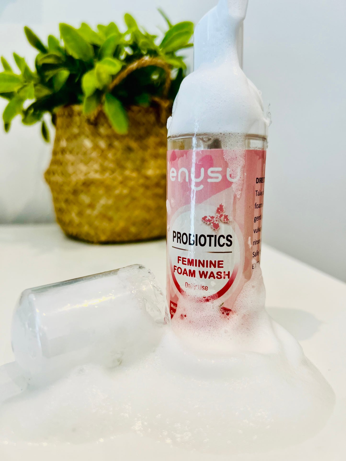 Bottle of enysu ladyblooom Probiotics Feminine Foam Wash on a white surface with a plant in the background.